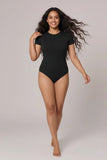 Woman wearing a black bodysuit on a plain background
