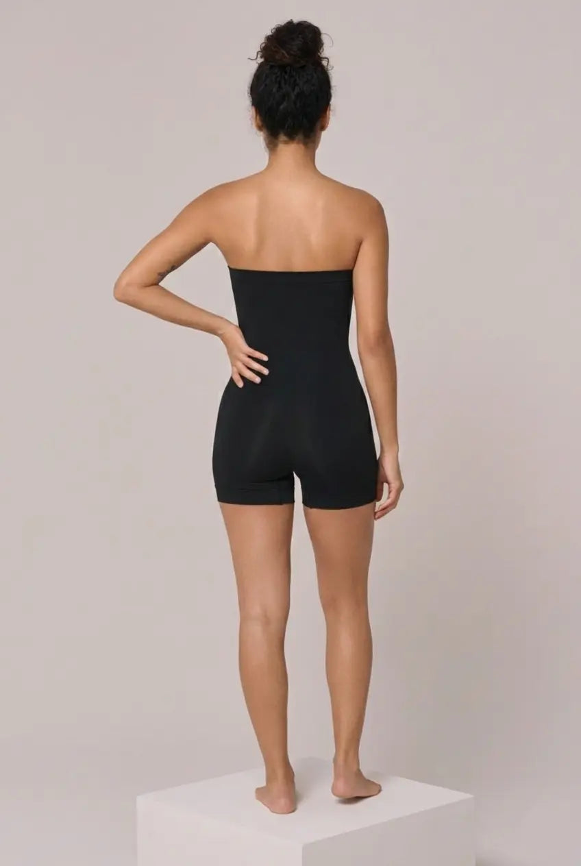 Woman wearing a black strapless romper on a plain background
