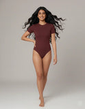 Woman wearing a maroon bodysuit against a plain background