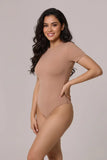 Woman wearing a beige bodysuit against a plain background